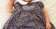 Josette joined the competition — help win amazing prizes! baby, infant, child, dress, floral_pattern, white_socks, lying_down, blanket, cute, portrait, smiling, skin, head, arms, legs, indoors, soft_light, clothing, person, young