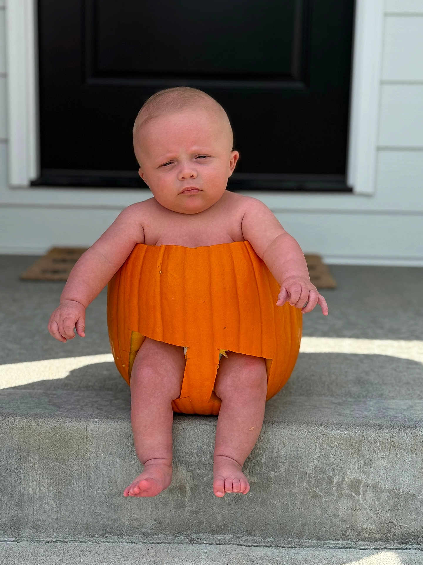 Liam is registered to the contest to win money with this photo: baby, pumpkin, porch, step, outdoor, expression, face, legs, feet, skin, door, concrete, holiday, fall, costume, child, sitting, front_door, funny, cute