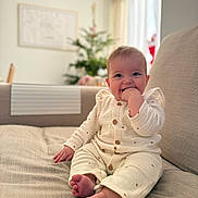 Lou a rejoint le concours — aidez-le/la à gagner de superbes lots ! baby, infant, smiling, sitting, cozy, indoors, couch, furniture, clothing, hand, feet, face, happy, home, holiday, christmas_tree, blurred_background, cute, child, portrait