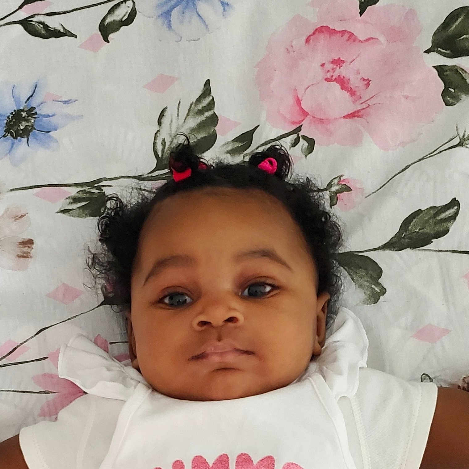 Axélia participe au concours pour gagner de l'argent avec cette photo : adorable, baby, background, child, comfort, cute, eyes, face, floral_blanket, hair, hair_ties, indoors, infant, lying_down, pattern, person, portrait, skin, white_clothing, young