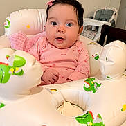 Luna is registered to the contest to win money with this photo: baby, infant, pink_clothing, onesie, inflatable_ring, dinosaur_print, bow, hair_accessory, wide_eyes, surprised_expression, indoor, high_chair, table, child, cute, seated, soft_toy, playful, colorful, portrait