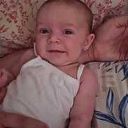Julia joined the competition — help win amazing prizes! baby, infant, smiling, white_clothing, hand, bed, bedding, pattern, floral_pattern, person, skin, arm, face, lying_down, comfort, cute, young_child, indoor, relaxed, happy
