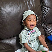 Jayden joined the competition — help win amazing prizes! toddler, child, boy, sitting, couch, leather, hat, bucket_hat, bow_tie, suspenders, green_outfit, socks, smiling, holding_object, indoor, furniture, happy, cute, casual_clothing, person