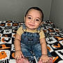 baby, child, smile, denim_overalls, yellow_shirt, barefoot, hands, feet, bed, blanket, halloween_theme, pumpkins, spiders, ghosts, black, orange, white, indoor, cute, portrait