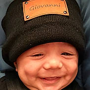 Giovanni is registered to the contest to win money with this photo: baby, smiling, black_hat, knit_hat, chubby_cheeks, infant, cute, happy, face, child, portrait, clothing, closeup, person, seatbelt, car_seat, young_child, skin, headwear, baby_smile