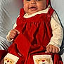 baby, infant, red_dress, headband, bow, smile, face, pockets, clothing, cute, lying_down, soft_surface, happy, child, festive, red, white, hand, cheeks, portrait