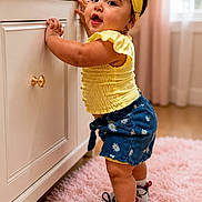 Josiris Isarel joined the competition — help win amazing prizes! toddler, child, yellow_headband, yellow_top, blue_shorts, floral_pattern, socks, shoes, pink_rug, cabinet, vase, flowers, indoor, curtains, wooden_floor, smiling, standing, baby, cute, home