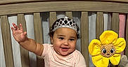 Josiris Isarel is registered to the contest to win money with this photo: baby, tiara, crib, plush_toy, minnie_mouse, flower_toy, smile, child, pink_clothing, bedding, curtains, indoor, happy, cute, sitting, toy, person, decor, soft_toys, infant