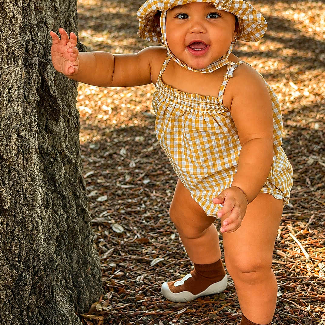 Josiris Isarel is registered to the contest to win money with this photo: child, toddler, hat, yellow, romper, tree, outdoor, nature, walking, sunlight, smiling, happy, baby, footwear, leaves, ground, person, cute, summer, playful
