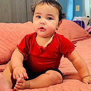 Josiris Isarel joined the competition — help win amazing prizes! baby, child, infant, red_shirt, bed, quilted_bedspread, indoor, portrait, sitting, cute, curly_hair, earring, skin, face, expression, home, furniture, window, natural_light, room