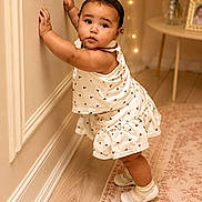 Josiris Isarel is registered to the contest to win money with this photo: toddler, child, standing, indoor, wall, white_clothing, dress, socks, shoes, carpet, table, flowers, vase, portrait, cute, baby, person, floor, earrings, decor