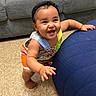 Josiris Isarel is registered to the contest to win money with this photo: baby, child, smiling, standing, colorful_clothing, headband, blue_ottoman, gray_couch, pillows, indoor, flooring, happy, cute, person, home, furniture, playful, toddler, expression, young_child