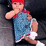 baby, infant, child, dress, flower_headband, red_hat, bracelet, sock, ruffle, couch, leather_sofa, sitting, portrait, cute, hand_in_mouth, stars_pattern, white_flowers, indoor, blue_dress, adorable