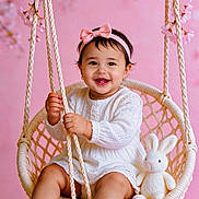 Josiris Isarel joined the competition — help win amazing prizes! baby, child, girl, swing, pink_bow, headband, smiling, white_dress, stuffed_animal, bunny, pink_background, flower, rope, happy, cute, portrait, indoor, soft_lighting, woven_swing, infant