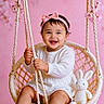 baby, child, girl, swing, pink_bow, headband, smiling, white_dress, stuffed_animal, bunny, pink_background, flower, rope, happy, cute, portrait, indoor, soft_lighting, woven_swing, infant