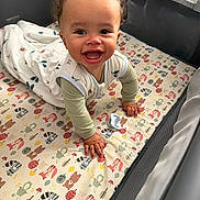 Torrin joined the competition — help win amazing prizes! baby, child, infant, smiling, laughing, crawling, playpen, nursery, mattress, blanket, pacifier, onesie, curly_hair, portrait, indoor, happy, face, hands, colorful, animal_pattern