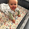 baby, child, infant, smiling, laughing, crawling, playpen, nursery, mattress, blanket, pacifier, onesie, curly_hair, portrait, indoor, happy, face, hands, colorful, animal_pattern