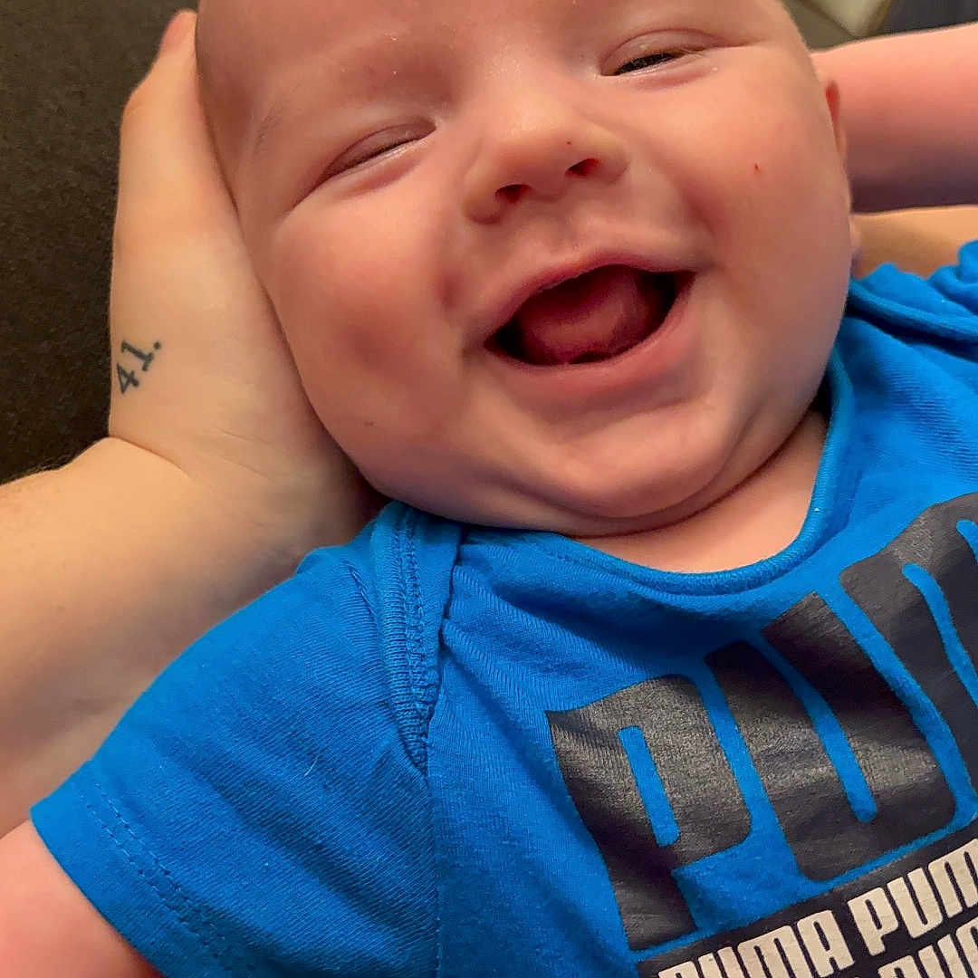 Kaydin is registered to the contest to win money with this photo: baby, babylaughing, bodypart, clothing, couch, face, finger, hand, happy, head, laughing, mouth, newborn, person, photography, portrait, skin, smile, t_shirt, tattoo
