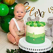 Caleb joined the competition — help win amazing prizes! baby, child, cake, birthday, balloons, green, gold, bow_tie, suspenders, plush_toy, elephant, celebration, floor, smiling, happy, party, decorations, white_stand, plant_leaves, indoor