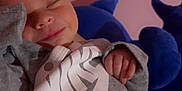 Wrenley is registered to the contest to win money with this photo: baby, sleeping, smile, nike, grey_clothing, plush_toy, pink_background, infant, peaceful, hand, face, cute, child, sleeve, soft_lighting, indoors, resting, cozy, smiley_face, hoodie