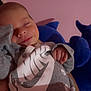 baby, sleeping, smile, nike, grey_clothing, plush_toy, pink_background, infant, peaceful, hand, face, cute, child, sleeve, soft_lighting, indoors, resting, cozy, smiley_face, hoodie