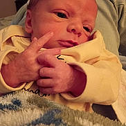 Tyson is registered to the contest to win money with this photo: baby, blanket, close_up, cozy, cute, expression, face, fingers, hand, indoor, infant, newborn, person, portrait, skin, sleepwear, soft_texture, warm_lighting, yellow_clothing, young_child