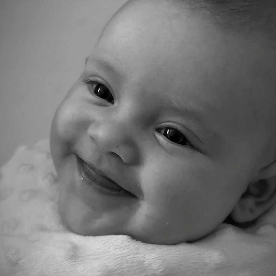 Charley is registered to the contest to win money with this photo: baby, black_and_white, blanket, cheeks, close_up, cute, expression, eyes, face, happy, head, infant, innocence, newborn, person, portrait, skin, smiling, soft_texture, tongue