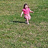 child, toddler, grass, outdoor, sunlight, smiling, happy, running, pink_clothing, shorts, nature, daytime, shadow, person, young_child, playful, greenery, summer, casual_wear, fun