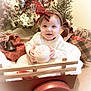 baby, child, red_bow, wagon, holiday, christmas, gift, wrapped_presents, wreath, decorations, carpet, smiling, white_sweater, ball, festive, indoor, cute, holiday_cheer, red, cozy