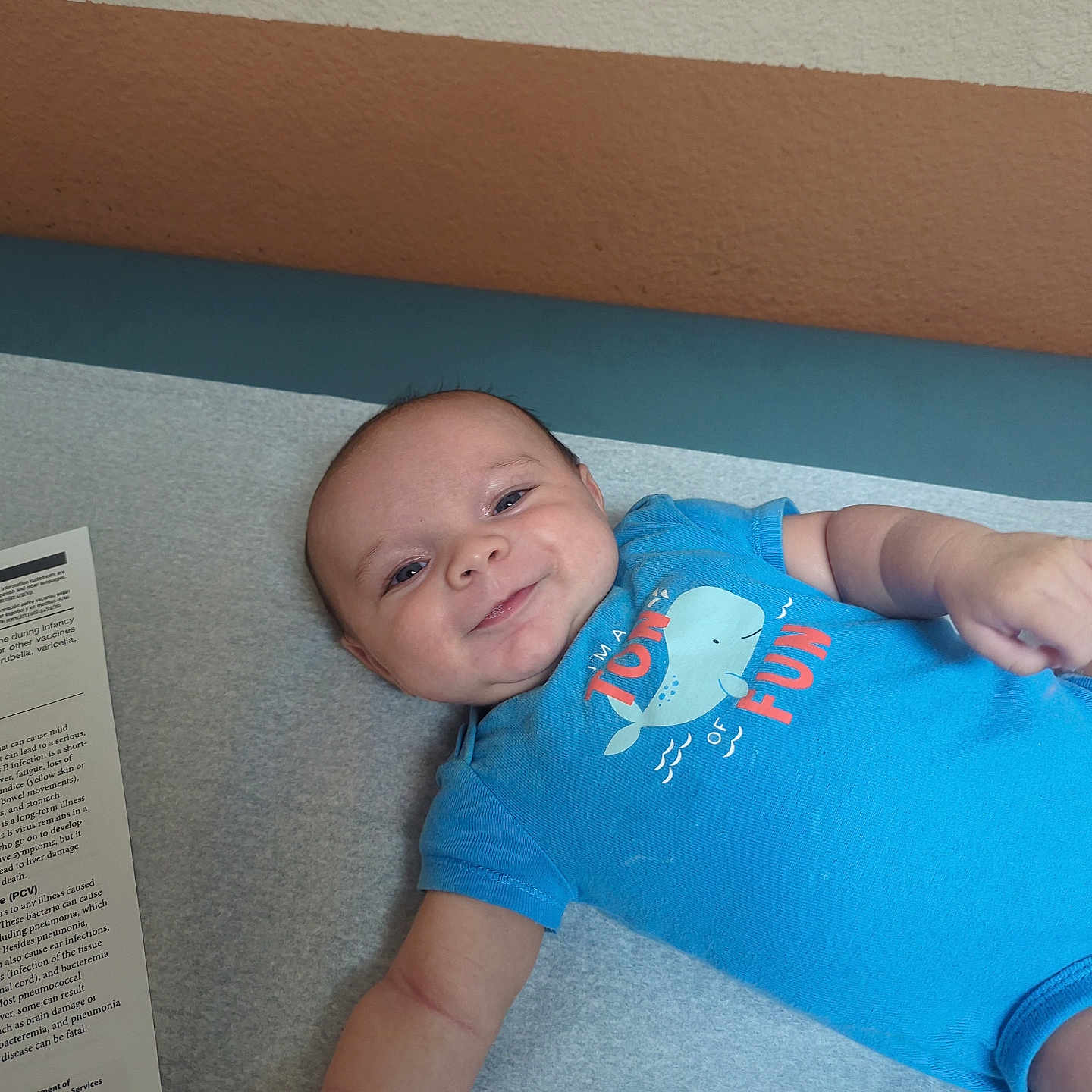 Dominic Sage Colon is registered to the contest to win money with this photo: arm, baby, blue_onesie, child, cute, face, happy, healthcare, indoor, infant, laying_down, medical_table, newborn, paper, person, short_sleeves, skin, smiling, wall, young