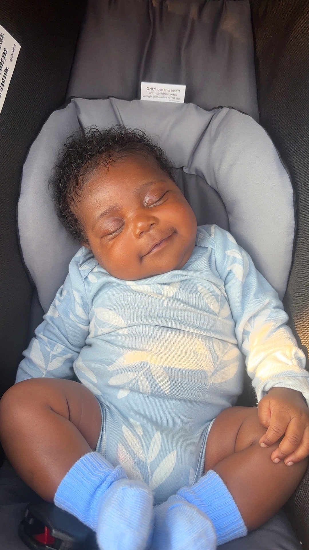 Treasure is registered to the contest to win money with this photo: baby, sleeping, smiling, curly_hair, car_seat, blue_outfit, socks, infant, child, peaceful, cute, cozy, clothing, toddler, resting, seat_belt, indoors, portrait, young_child, relaxed