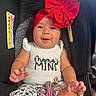 baby, child, car_seat, headband, red_bow, white_shirt, printed_text, smiling, happy, infant, cute, sitting, clothing, patterned_pants, accessory, indoor, portrait, person, young_child, closeup