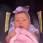 Sonia is registered to the contest to win money with this photo: baby, infant, car_seat, blanket, pink, purple, headband, clothing, cute, child, person, portrait, seat, warning_label, soft_texture, indoor, closeup, holding, young, face