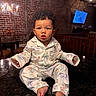 Asaiah is registered to the contest to win money with this photo: toddler, child, pajamas, curly_hair, indoor, countertop, brick_wall, chandelier, dining_room, table, chair, foot, face, expression, person, lighting, home_interior, cute, sitting, portrait