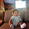 baby, child, infant, sitting, couch, indoor, hat, striped_clothing, white_socks, face, curious_expression, furniture, television, blurred_background, cozy, warm_lighting, person, portrait, young_child, home