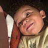 Asaiah is registered to the contest to win money with this photo: child, toddler, smile, face, curly_hair, pillow, close_up, expression, indoors, soft_lighting, yellow_shirt, leaf_pattern, skin, cheek, happy, portrait, person, young_child, cute, laying_down