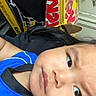 Liam is registered to the contest to win money with this photo: child, face, person, blue_shirt, cardboard_box, indoors, young_child, expression, black_hair, skin, reclining, closeup, cheeks, casual_clothing, background, damaged_wall, yellow, red_text, serious, portrait