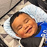 baby, smile, stroller, blue_outfit, cushion, happy, infant, child, face, portrait, comfort, hand, bracelet, indoor, baby_accessory, seat, closeup, head, cute, resting
