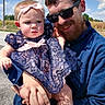 Charlie is registered to the contest to win money with this photo: baby, man, child, holding, outdoor, blue_sky, clouds, dress, lace, bow, sunglasses, beard, happy, portrait, family, person, casual_clothing, road, nature, sunlight