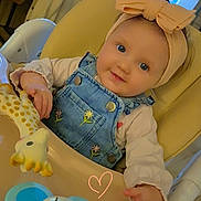 Livia participe au concours pour gagner de l'argent avec cette photo : baby, infant, highchair, headband, bow, denim_overalls, toy, giraffe_toy, elephant_toy, blue_eyes, smiling, rosy_cheeks, hand, feeding_table, indoor, kitchen, cozy, portrait, cute, doodle_heart