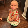 toddler, child, smiling, sitting, floor, wooden_floor, indoor, clothing, colorful, leggings, top, barefoot, face, happy, person, home, chair, backpack, earring, young_child