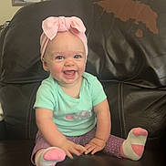 Joani is registered to the contest to win money with this photo: baby, child, smiling, headband, pink, sitting, leather_chair, indoor, happy, cute, portrait, sock, purple_pants, green_shirt, home, decor, clock, framed_photos, furniture, person