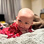 Sutton is registered to the contest to win money with this photo: baby, infant, smiling, tongue_out, red_clothing, blanket, soft_texture, face, head, cheeky, happy, indoors, blurred_background, person, cute, young_child, playful, cozy, lying_down, expression