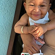 Danaria joined the competition — help win amazing prizes! baby, smile, child, arm, bracelet, clothing, hand, leg_warmer, person, skin, sunlight, texture, wall, holding, cute, happy, infant, portrait, outdoor, colorful