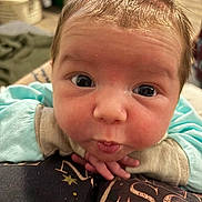 Kai is registered to the contest to win money with this photo: baby, infant, close_up, face, eyes, cheeks, newborn, chin, hands, clothing, onesie, expression, surprised, indoors, blanket, hair, portrait, skin, gaze, pout