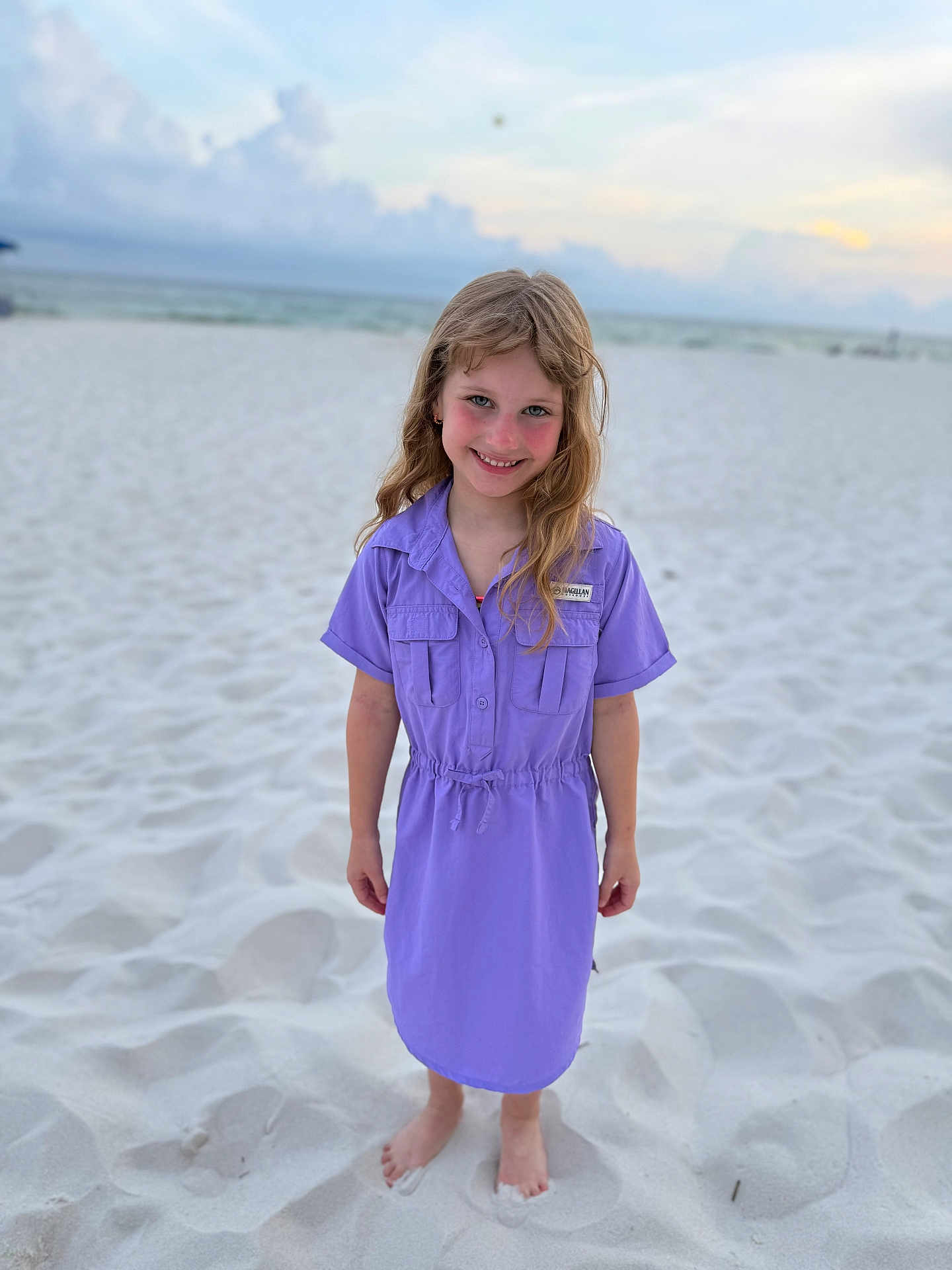 Rhegan is registered to the contest to win money with this photo: child, girl, beach, sand, sea, ocean, sky, clouds, dress, barefoot, smile, blond_hair, portrait, outdoor, summer, vacation, young, happy, casual_clothing, nature