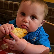 Reginald Iv joined the competition — help win amazing prizes! baby, child, bread, food, blue_shirt, tablecloth, checkered, face, hands, eating, restaurant, highchair, curious, messy, indoor, person, closeup, young, plump, cute