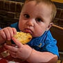 baby, child, bread, food, blue_shirt, tablecloth, checkered, face, hands, eating, restaurant, highchair, curious, messy, indoor, person, closeup, young, plump, cute