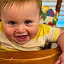 baby, child, smiling, face, eyes, hand, wooden_table, clothing, yellow_shirt, indoor, high_chair, colorful_background, happy, portrait, cute, infant, person, toddler, expression, closeup