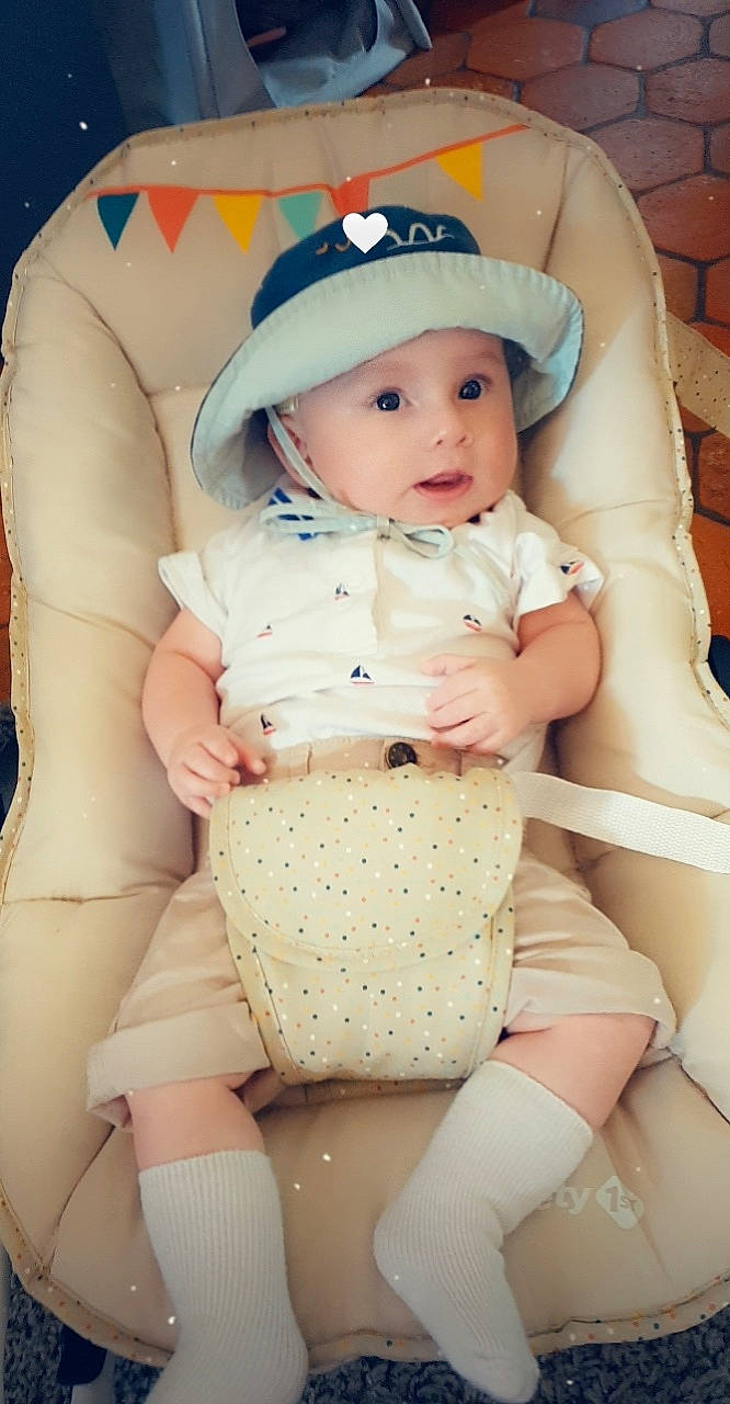 Gabriele participe au concours pour gagner de l'argent avec cette photo : arm, baby, baby_toddler_clothing, cap, cheek, comfort, eye, finger, hand, head, headwear, lap, leg, mouth, organ, person, pink, product, skin, stomach